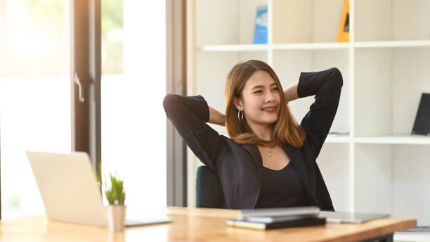 istock Gorgeous office woman relaxing by stretching her body while sitting in front her computer laptop at the wooden working desk over comfortable living room as background. 1221175896