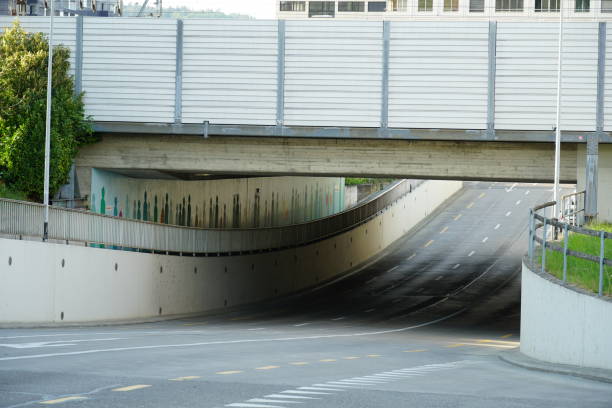 istock Railway bridge with traction lines and a noise protection wall closeup. Under it there is a multilane road with sidewalks. Modern residential buildings stand in the background. 1221178719