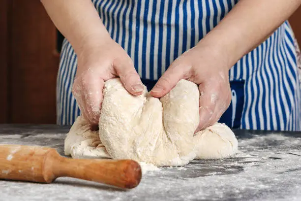 Female hands knead the dough on a floury table. The concept of home cooking.