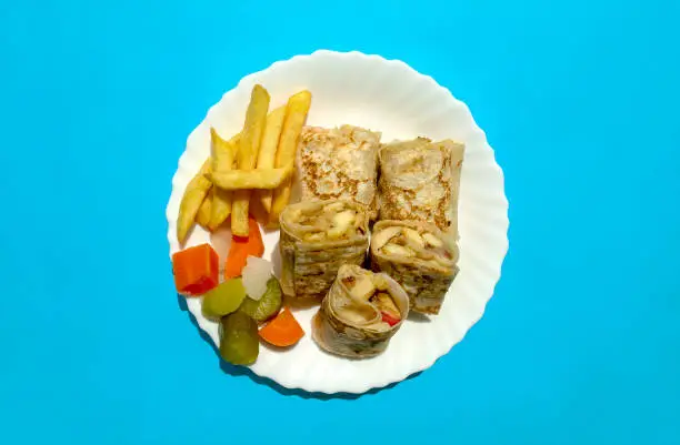 Photo of Arabic chicken shawarma plate with fried fries and pickled vegetables on blue background.
