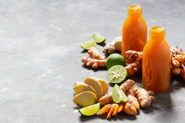 Photo of Healthy drink from turmeric and ginger roots and lime in small bottles on grey concrete background.