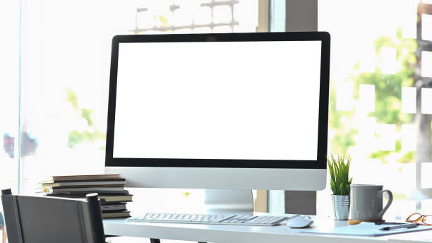 istock Computer monitor putting on white working desk surrounded by coffee cup, potted plant, document, stack of books, wireless keyboard and mouse over modern office as background. 1221202189