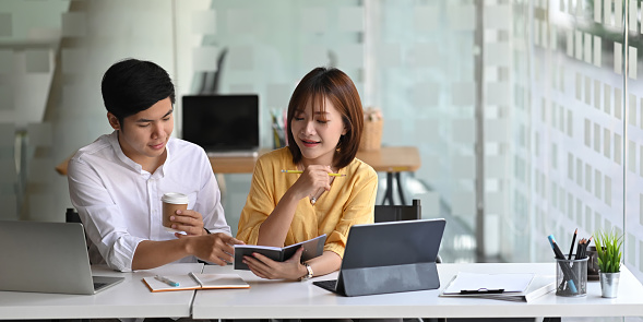 Photo of business consulting team working together with computer tablet while sitting at the long working desk over modern office as background.