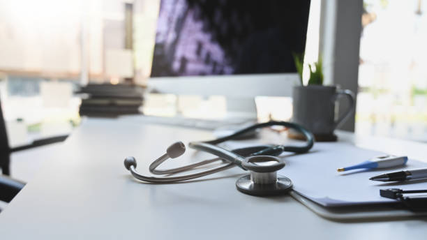 Stethoscope putting on doctor working desk surrounded by clipboard, thermometer, pen, coffee cup, stack of book and computer monitor. Doctor workspace concept.