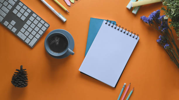 istock Top view image of coffee cup putting on colorful working desk surrounded by computer keyboard, note, pencils, pen, flowers pine cone, and marker pens. Cluttered workspace concept. 1221202351
