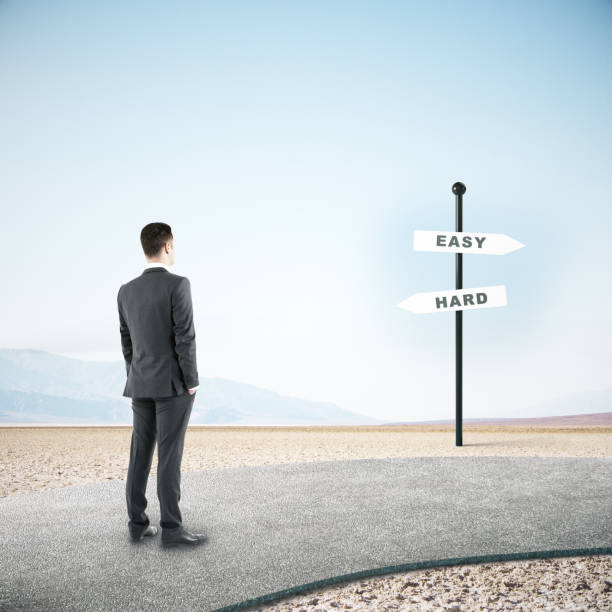 istock businessman standing on road and looking on easy and hard sign post. 1221204898