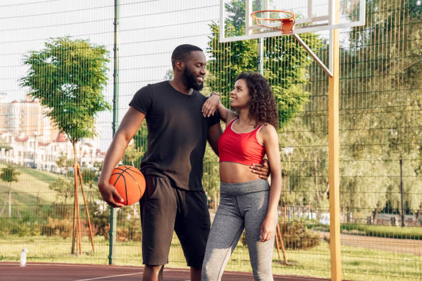 Perfect Team. African couple standing with ball hugging on basketball court looking at each other happy