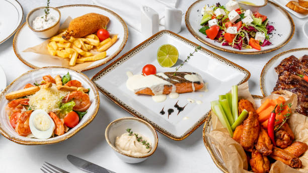istock Assorted dishes on table. Salmon steak on the grill, chicken wings, caesar with shrimps, kiev cutlet with fries, greek salad 1221206441