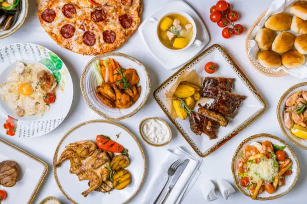 Assorted dishes on table. Barbecue pork ribs, chicken wings, pasta carbonara, pizza pepperoni, fish soup, chicken tabaka, steak file minion and caesar with shrimps top view