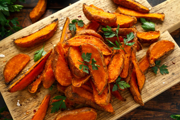 Healthy Baked Orange Sweet Potato wedges with dip sauce, herbs, salt and pepper on wooden board Healthy Baked Orange Sweet Potato wedges with dip sauce, herbs, salt and pepper on wooden board. sweet potato photos stock pictures, royalty-free photos & images