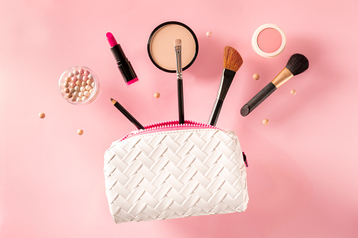 Professional makeup, flying out of a bag, on a pink background. Lipstick, brushes, powder compact, a creative beauty design