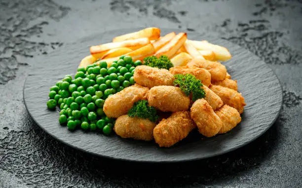Crispy Battered scampi nuggets served on slate plate with potato chips and green peas.
