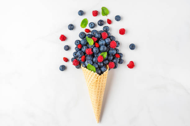 istock Fresh summer blueberries and raspberries with mint in waffle cone on white marble background. flat lay. top view 1221210834