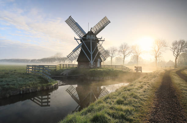 ветряная мельница в тумане по реке и дороге - netherlands windmill farm farmhouse стоковые фото и изображения