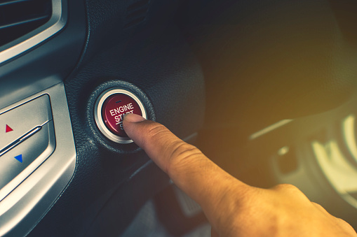 Hand of car driver press to the engine start/stop button for engine ignition in a luxury car.
