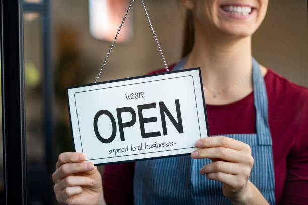 Open sign in a small business shop Small business owner smiling while turning the sign for the reopening of the place after the quarantine due to covid-19. Happy businesswoman standing at her restaurant or coffee shop gate with open signboard. Close up of woman"u2019s hands holding sign now we are open support local business. opening stock pictures, royalty-free photos & images