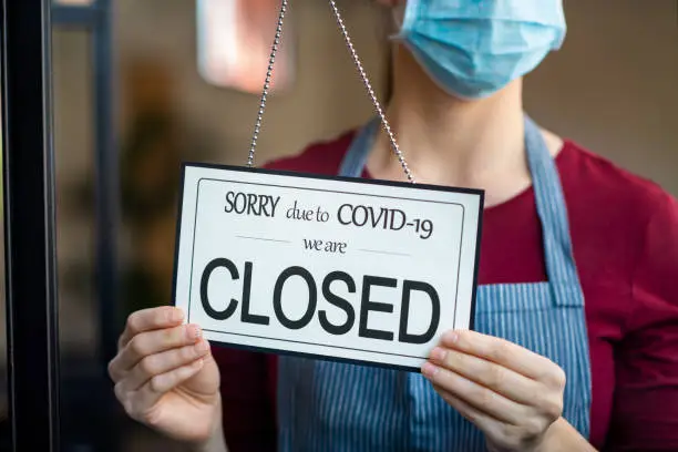 Businesswoman closing her business activity due to covid-19 lockdown. Owner with surgical mask close the doors of her store due to quarantine coronavirus damage. Close up sign of bankrupt business due to the effect of COVID-19 pandemic.