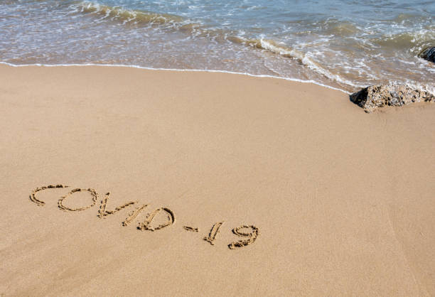 istock COVID-19 written in sand on a beach with the sea 1221213696