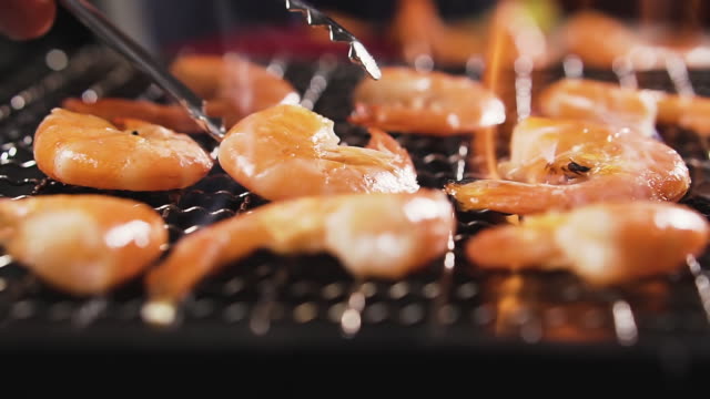 Tongs overturn shrimps that are fried on fire.