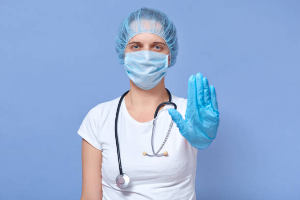 istock Image of confident responsible female standing isolated over blue background in studio, wearing uniform, medical mask and gloves, raising one hand, fighting against coronavirus. Epidemic concept. 1221214553