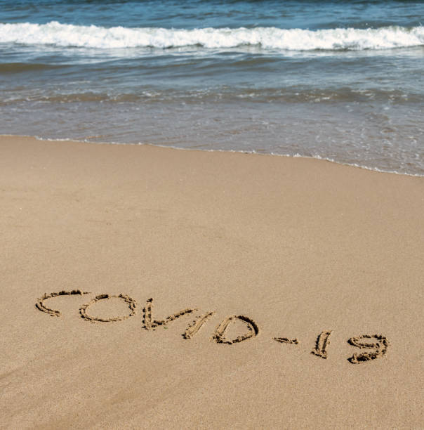 istock COVID-19 written in sand on a beach with the sea 1221214604