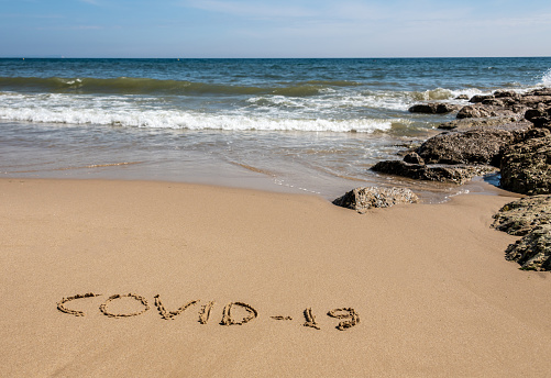 COVID-19 written in the sand on a beach with the sea