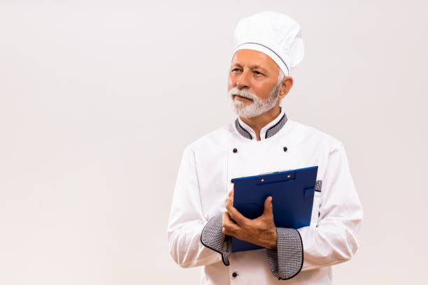 istock Senior  chef holding cookbook and thinking 1221214982