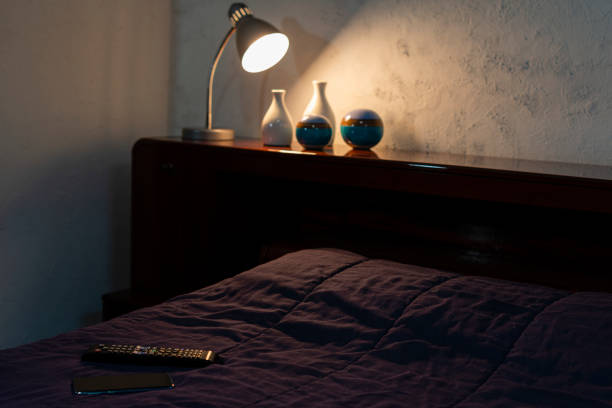 istock light fixture illuminating objects on the headboard and control and cell phone on duvet. Home interior. Selective focus 1221216121