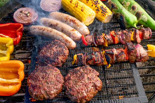 Peppers, Green Chilies, Corn, Onion, Hamburgers, Brats, and Kabobs arranged on a charcoal grill