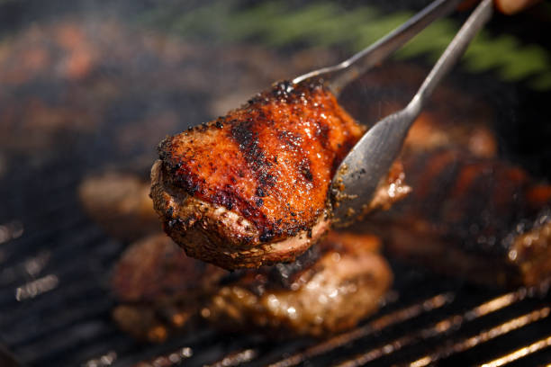 トングはバーベキューで焼いたアヒルの胸の切り身とチキンドラムスティックを保持します - barbecue grill chicken barbecue chicken breast ストックフォトと画像