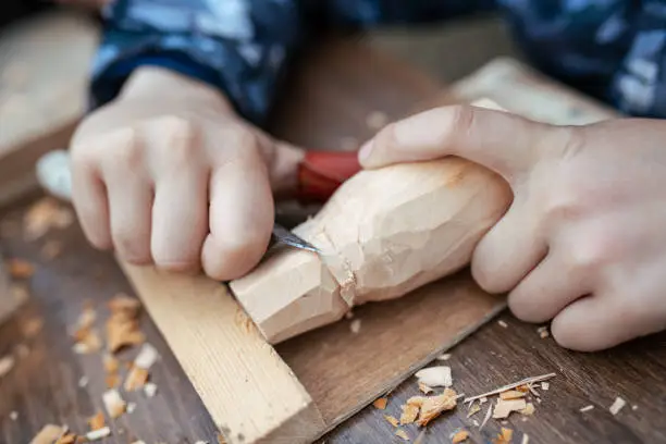 child carves a toy in wood with a knife.  carpenter in the workshop. Close-up of hands