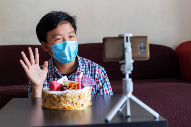 Young boy wearing facemask, doing teleconference celebrating birthday