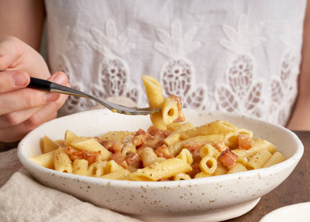 istock Carbonara pasta. Woman sits at table and eats pasta penne with pancetta, 1221223897