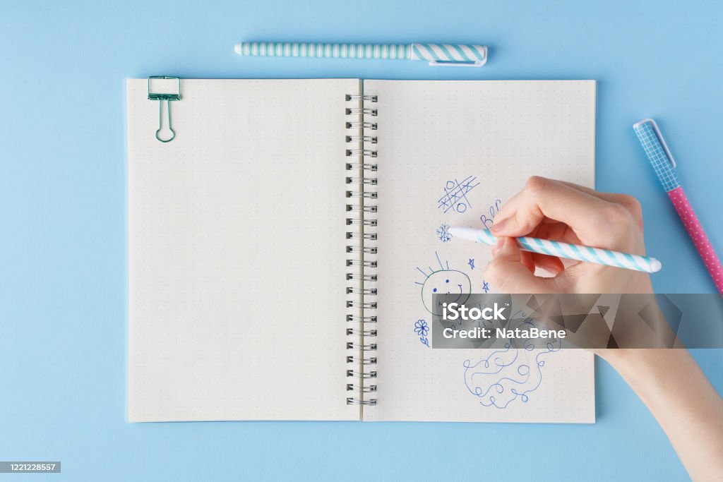 Hand draws scribble in a notebook. Blank notepad page in bullet journal Hand draws scribble in a notebook. Blank notepad page in bullet journal on bright blue office desktop. Top view of modern table with notebook, stationery. Mock up, copy space Doodle Stock Photo