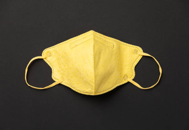 istock Yellow medical mask on black paper background flat lay 1221234908