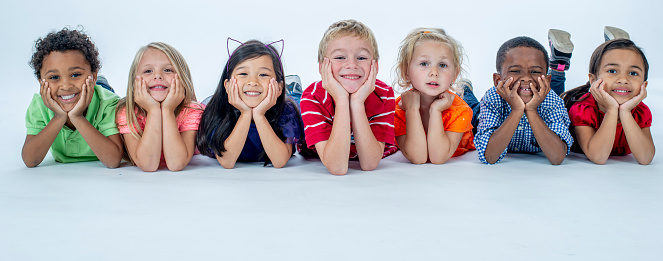Multi-ethnic group of elementary age children laying in a row posing and smiling at the camera.