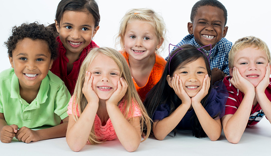 Multi-ethnic group of elementary age children laying in a row posing and smiling at the camera.