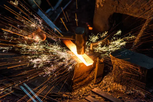 Blacksmith manually forging the molten metal on the anvil with spark fireworks