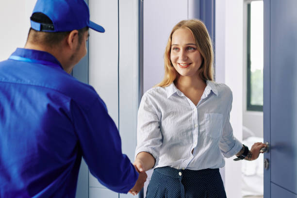 Young woman greeting repairman Smiling beautiful young woman opening entrance door and greeting repairman door repairman men manual worker stock pictures, royalty-free photos & images
