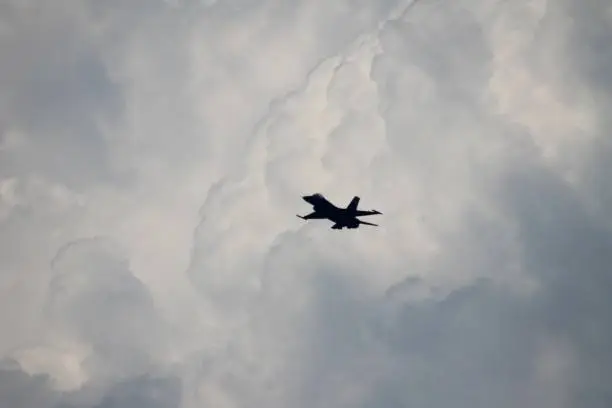 Silhouette of an F-18 in flight with a background of dramatic clouds