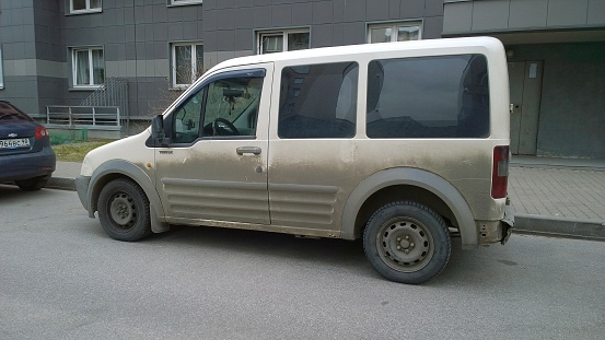 St. Petersburg, Russia - April 6, 2020: Old dirty white car Ford Transit Connect T220LX parked on a road near an apartment building. Washing vehicle exterior. Protection and painting auto concept.