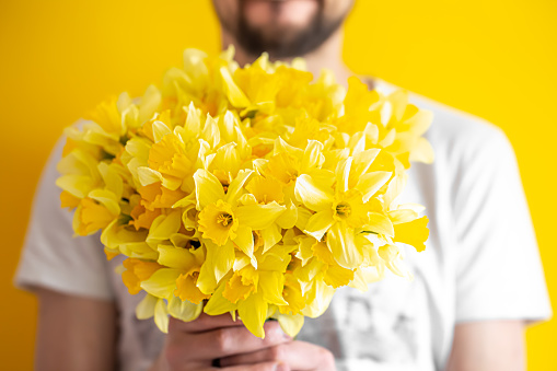 Hipster-a man on a yellow background in a shirt and a large bouquet of daffodils. The concept of greetings and women's day.