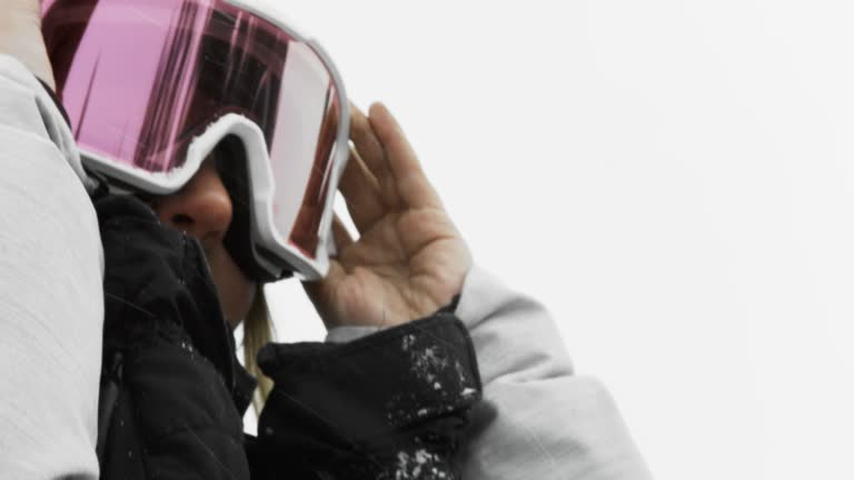 A Smiling Teenaged Female Snowboarder Puts on Her Goggles in Preparation of Snowboarding on an Overcast Winter Day