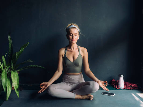 yoga at home: beautiful blonde woman meditating in the lotus position while listening to music - yoga meditating women exercise mat imagens e fotografias de stock