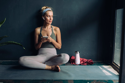 Home workout sessions: fit blonde woman in sportswear texting on her mobile phone after working out.