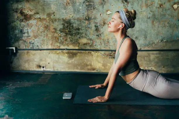 Self care rituals:  woman wearing wireless earphones using her mobile phone during her yoga practice.