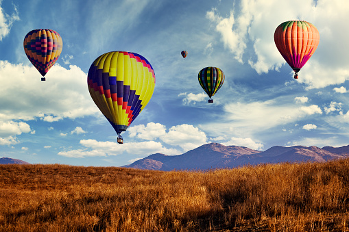 Two hot air balloons are just beginning to rise and float above the Namib Desert at sunrise.