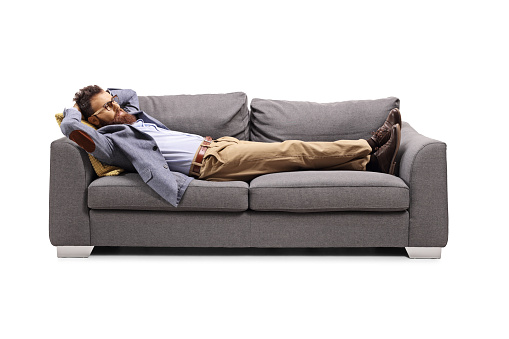 Bearded man lying on a gray sofa isolated on white background