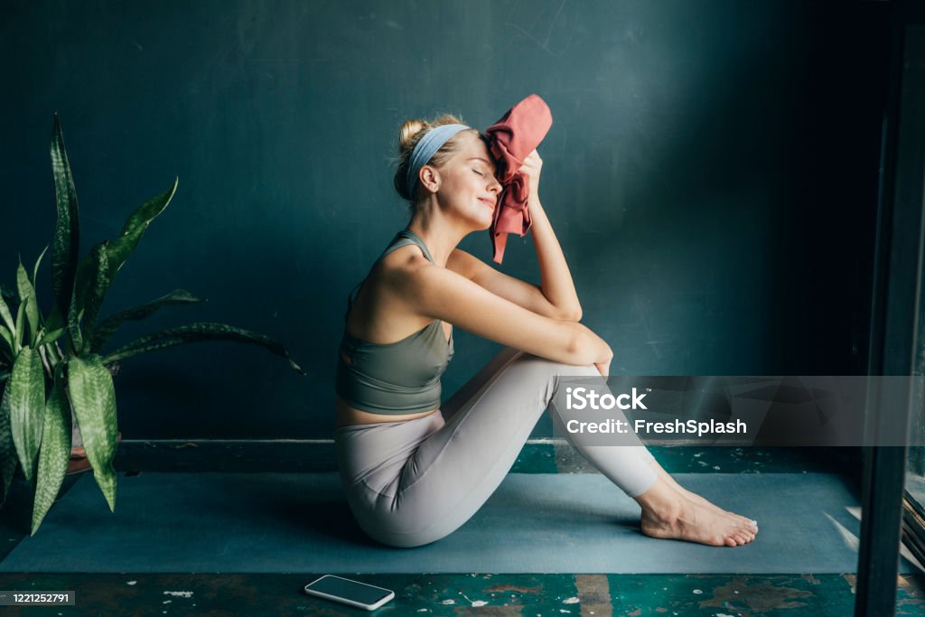 Tired, but Happy: Fit Blonde Woman Wiping her Face with a Towel after a Home Workout Smiling woman wiping off sweat with a towel after a home workout. Exercising Stock Photo