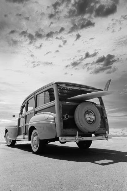 Black and White Woody Surf Car This is a black and white photograph of a surfer wood car parked at the beach watching the morning sunrise surfboard fin stock pictures, royalty-free photos & images